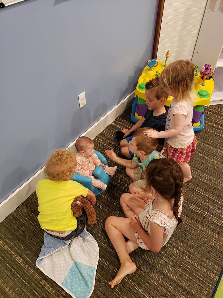 Children sitting on the floor around a baby in a bouncer