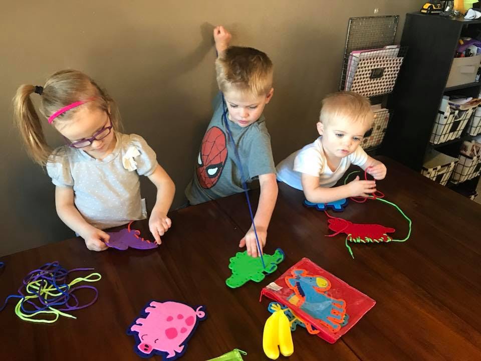 Three children playing with lacing toys at a table