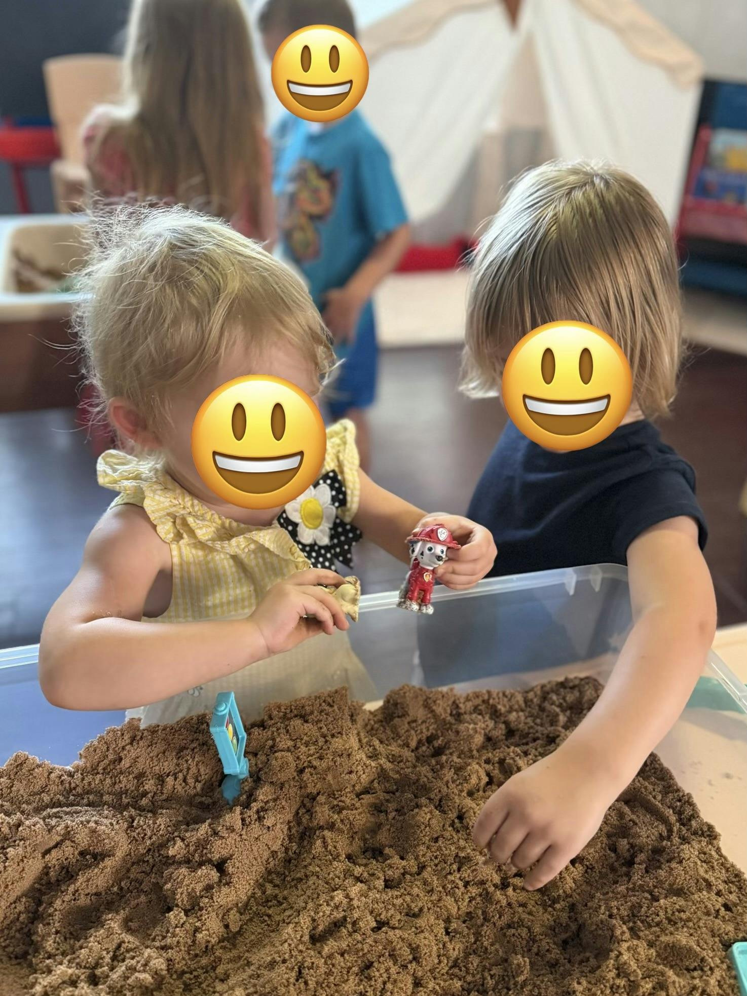 Children playing with small toy figures in a container of kinetic sand
