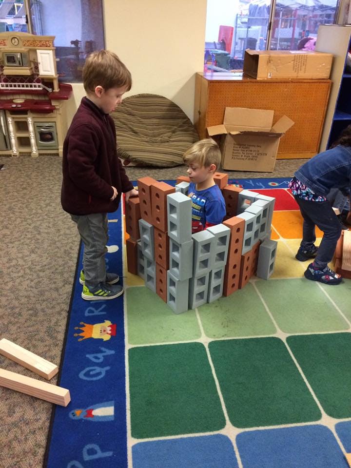 Two children playing with building blocks on a colorful rug