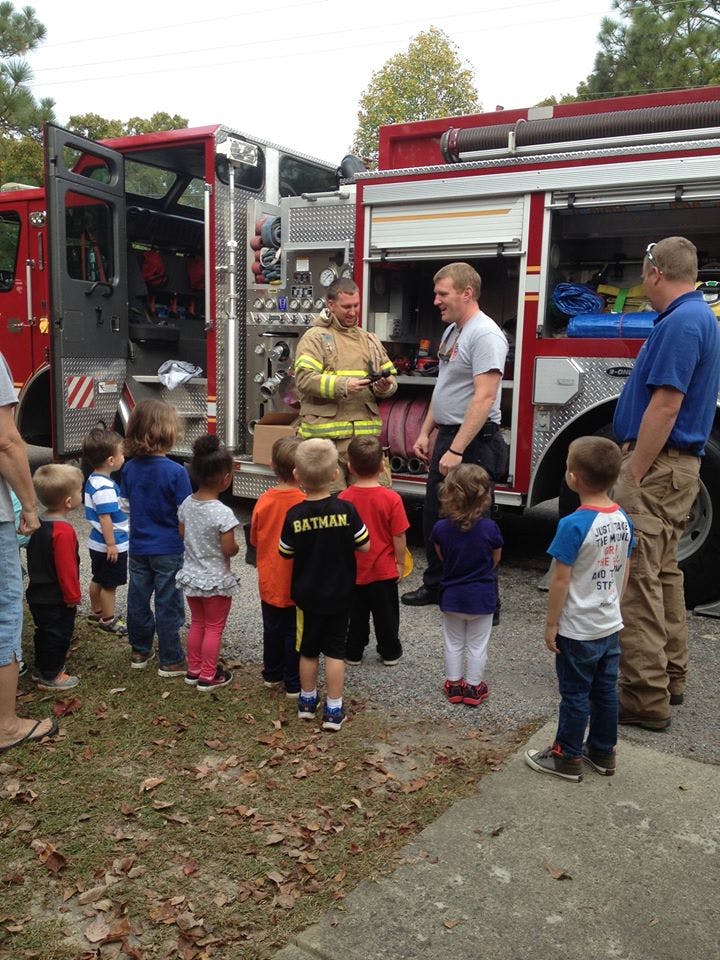 Firefighter showing equipment to a group of children and adults near a fire truck