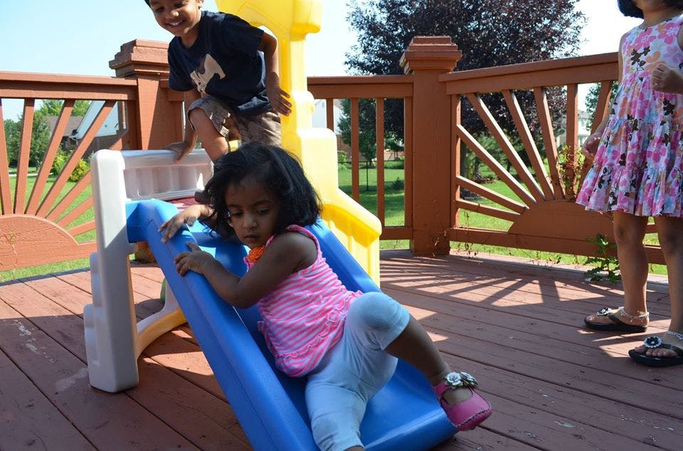 Child on a blue slide with another child standing nearby