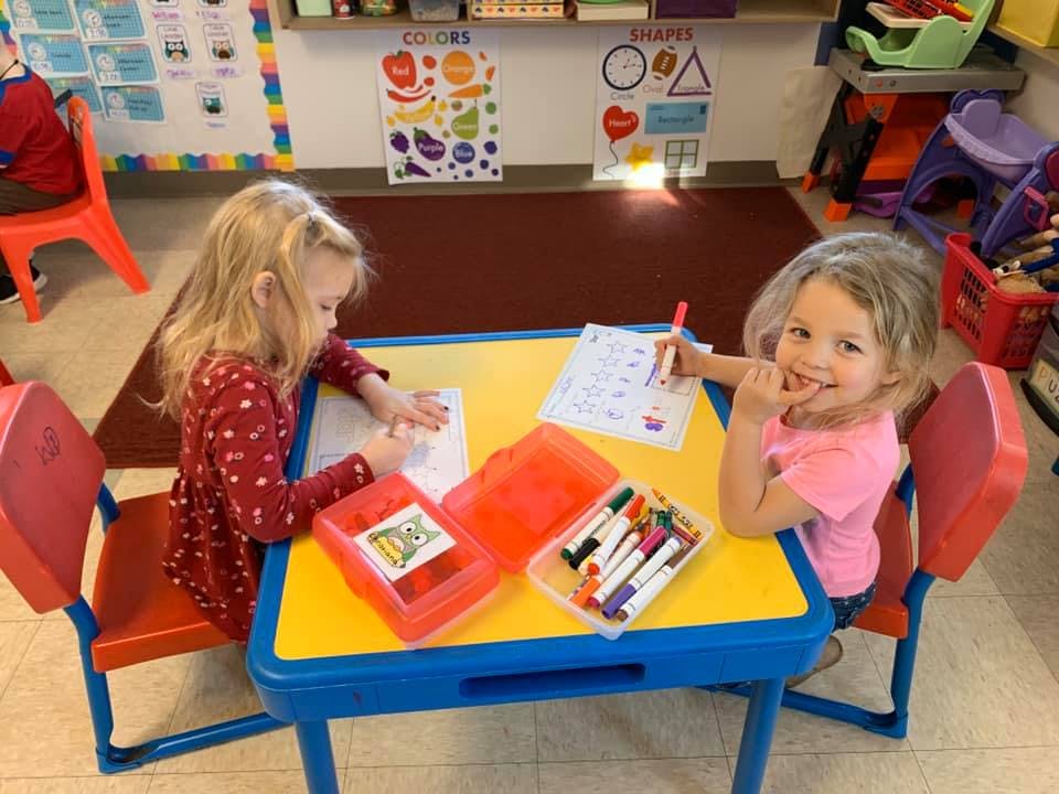 Two children drawing at a small table in a classroom