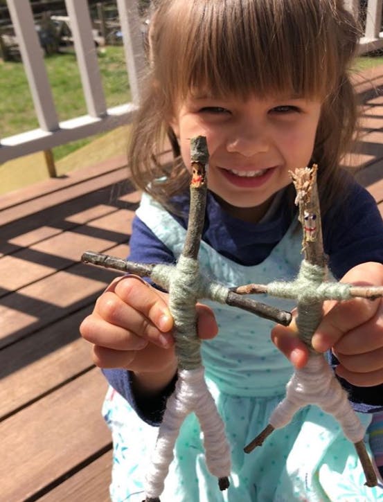 Child holding two stick figures wrapped in yarn