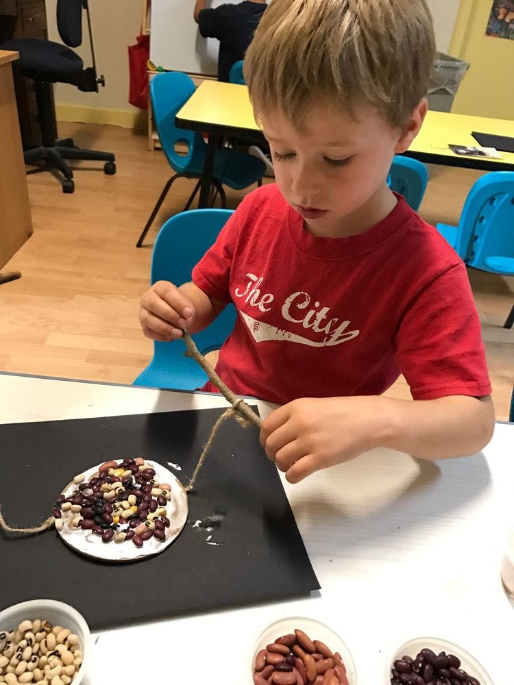 Child working on a craft with beans and string
