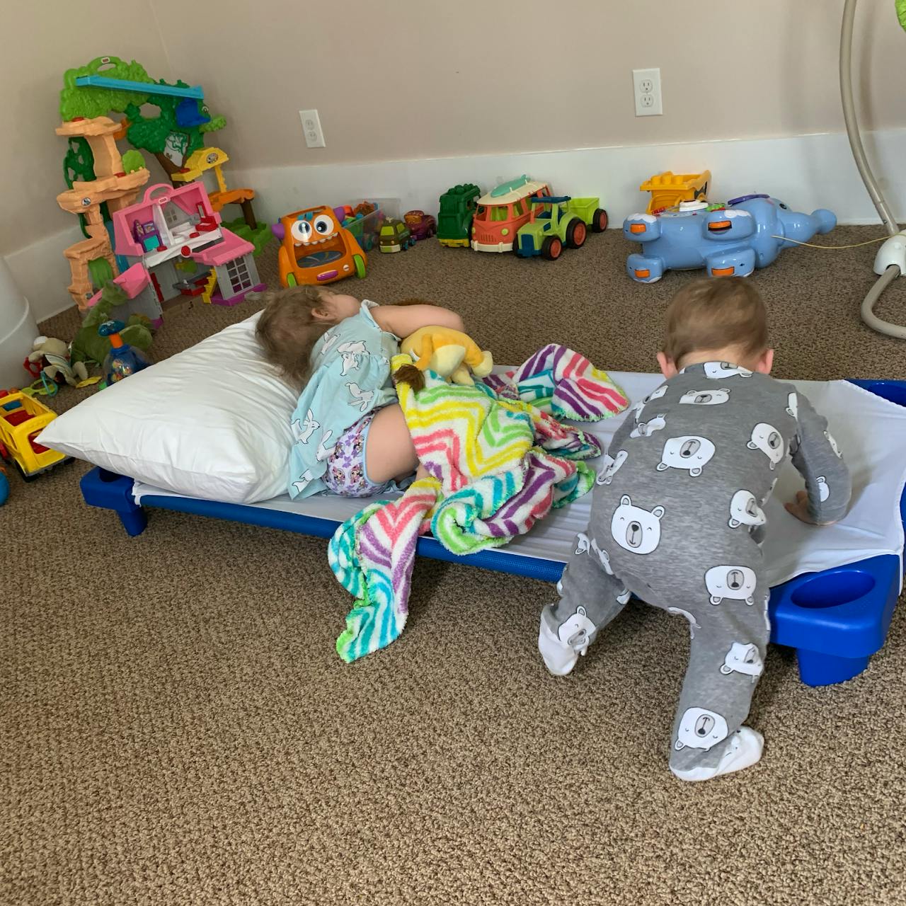 Child sleeping on a cot while another child crawls nearby