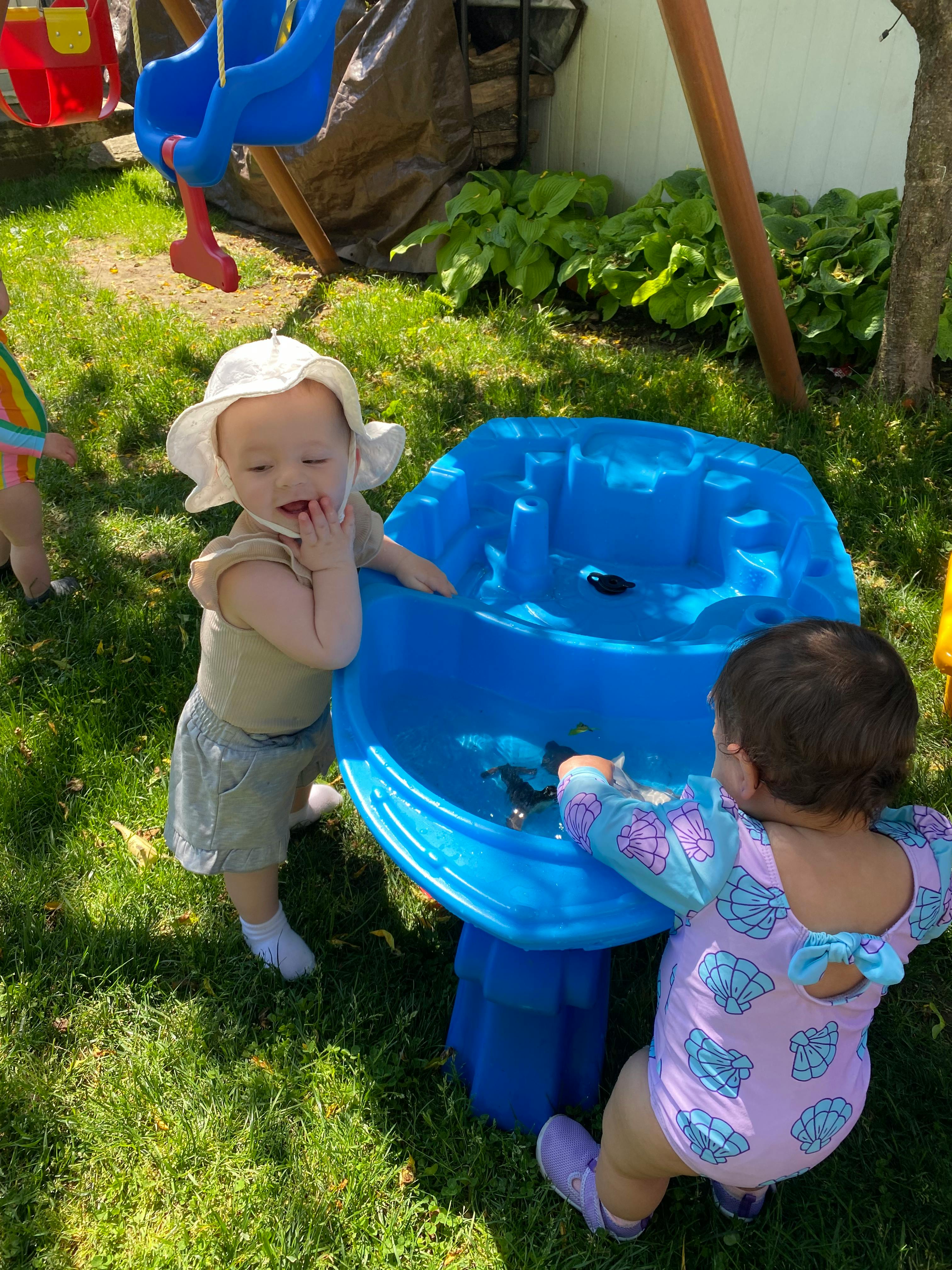Two children playing with a blue water table outdoors