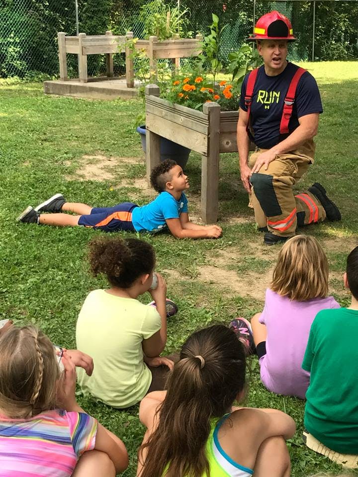 Person in firefighter gear kneeling in front of children on grass