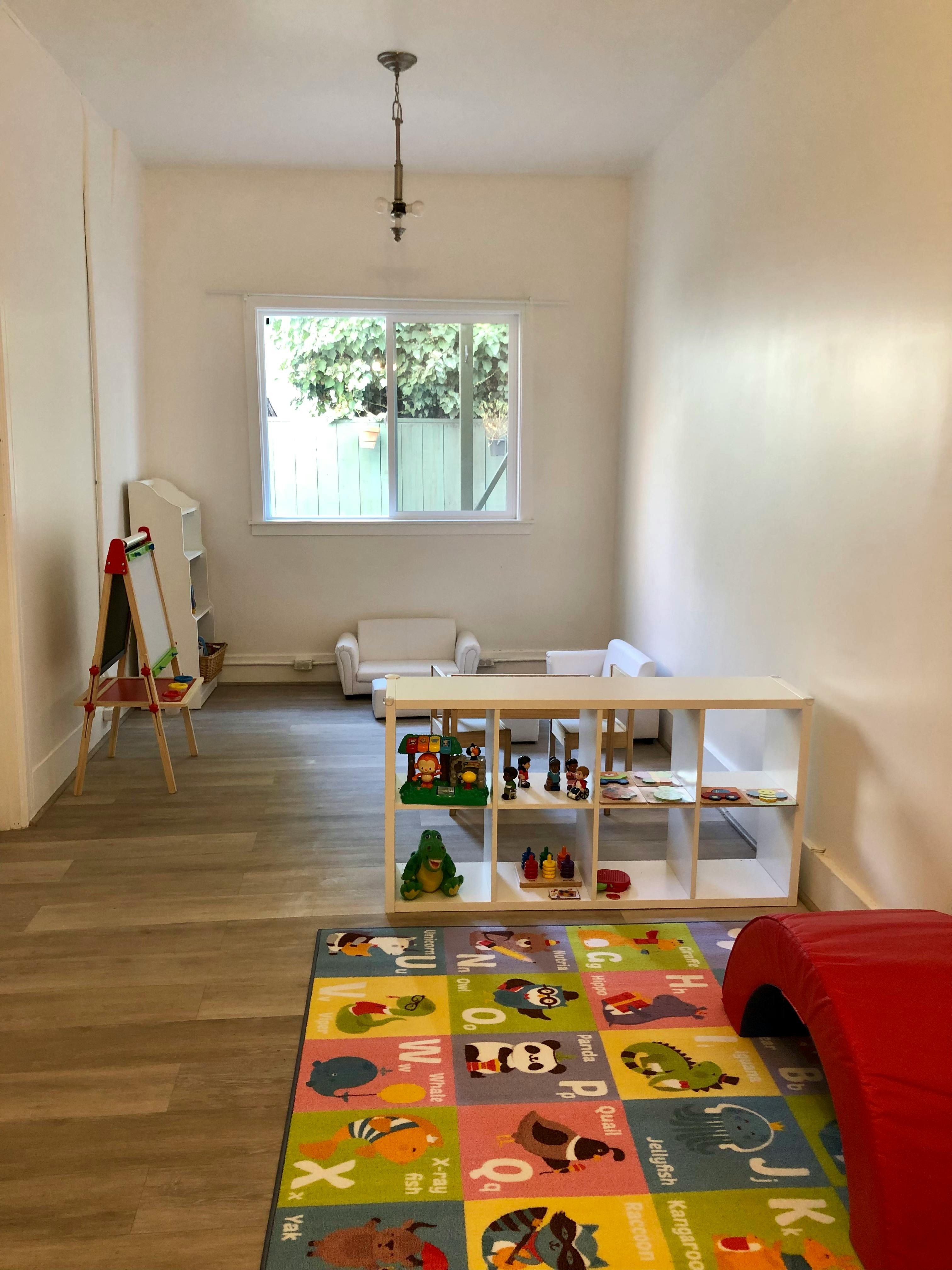 Playroom with a colorful alphabet rug, toy shelf, and easel