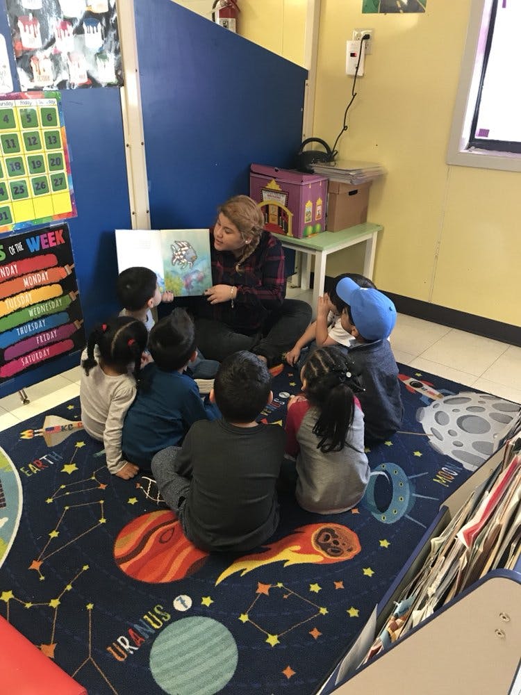 Person reading a book to a group of children in a classroom