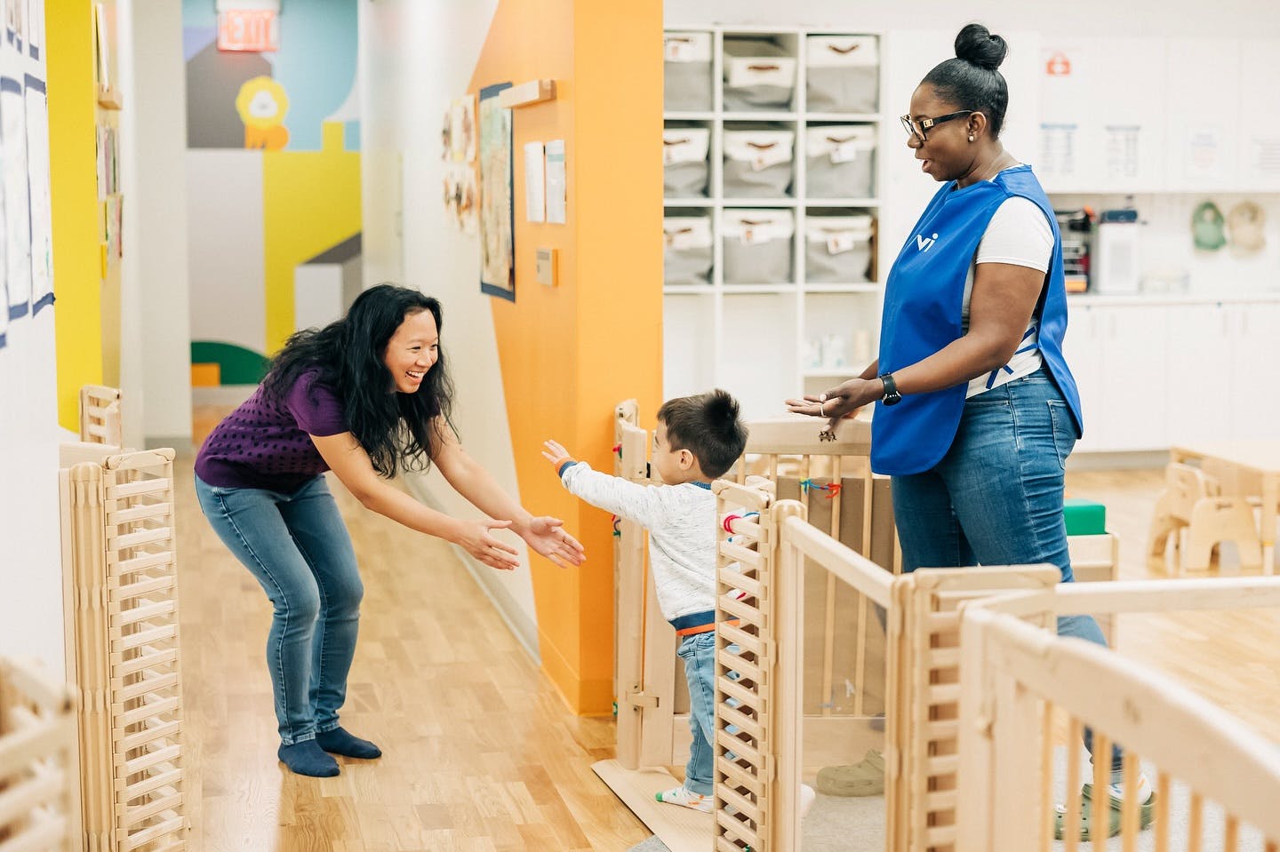 Person reaching out to a child in a play area, another person standing nearby