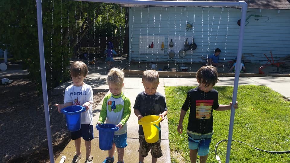 Children playing with buckets under a water sprinkler