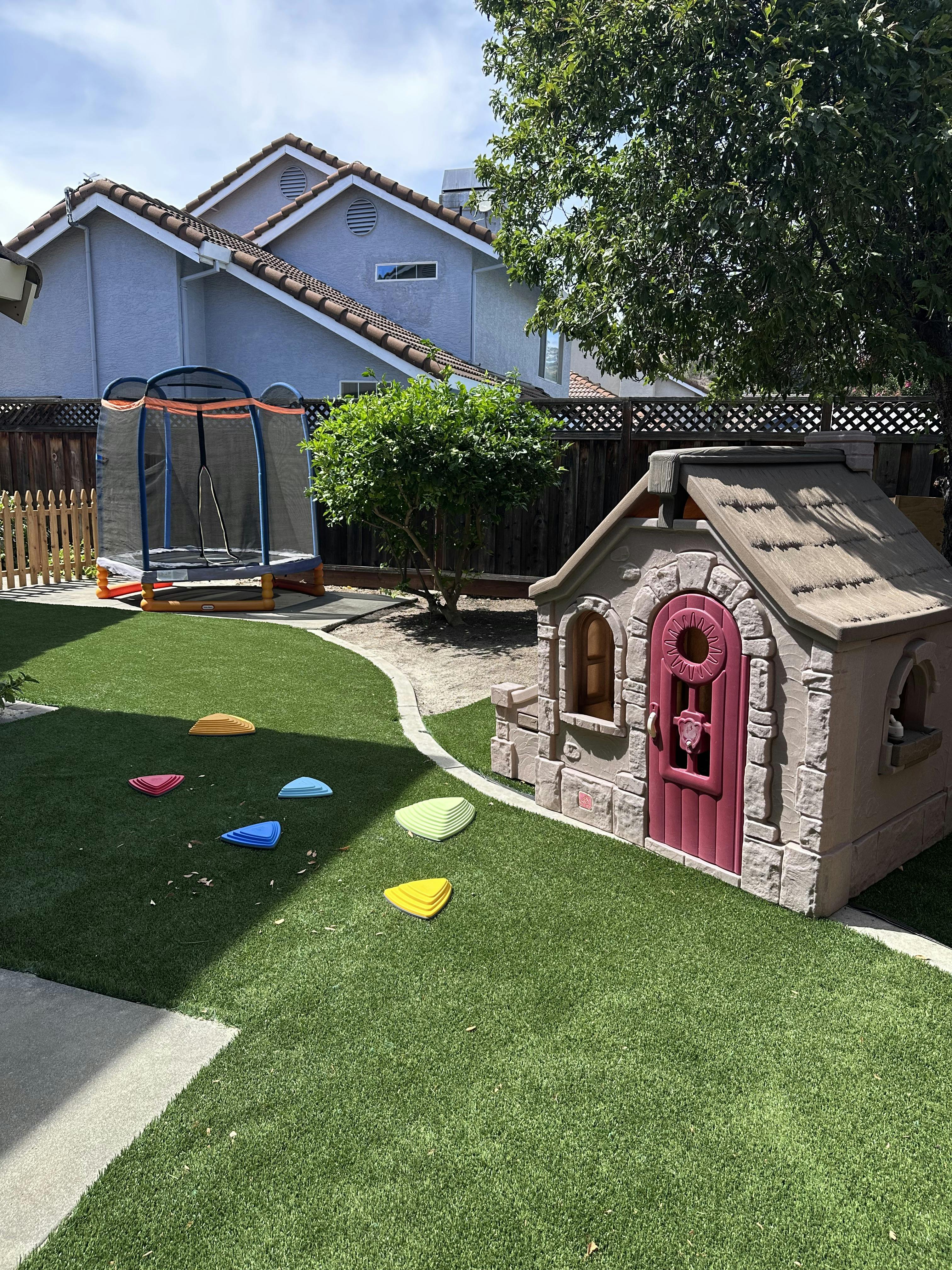 Playhouse and small trampoline in a backyard with stepping stones on the grass