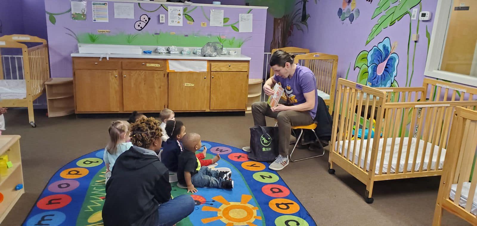 People and children sitting on a rug in a room with cribs