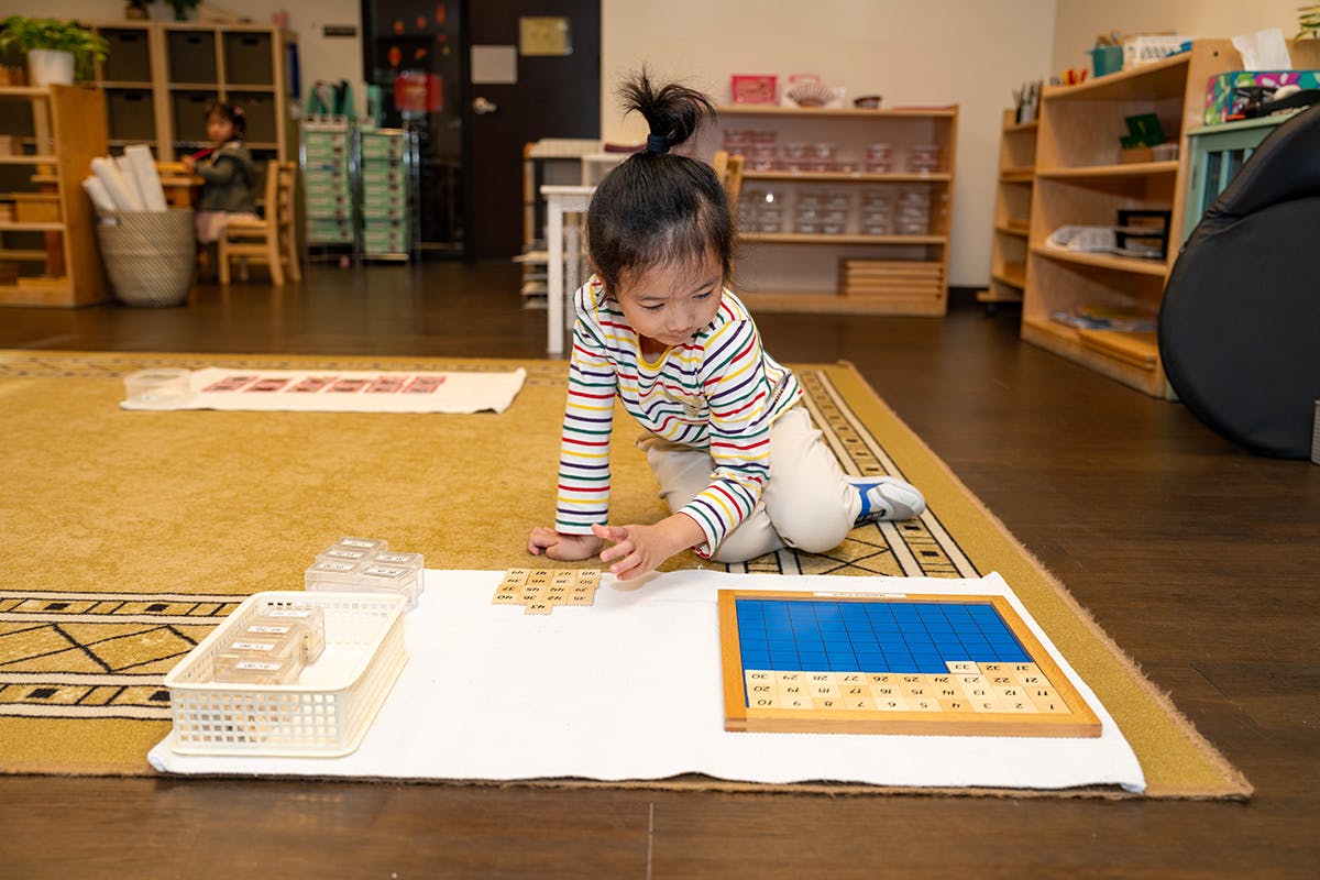 Child on floor playing with wooden blocks and blue puzzle in a classroom