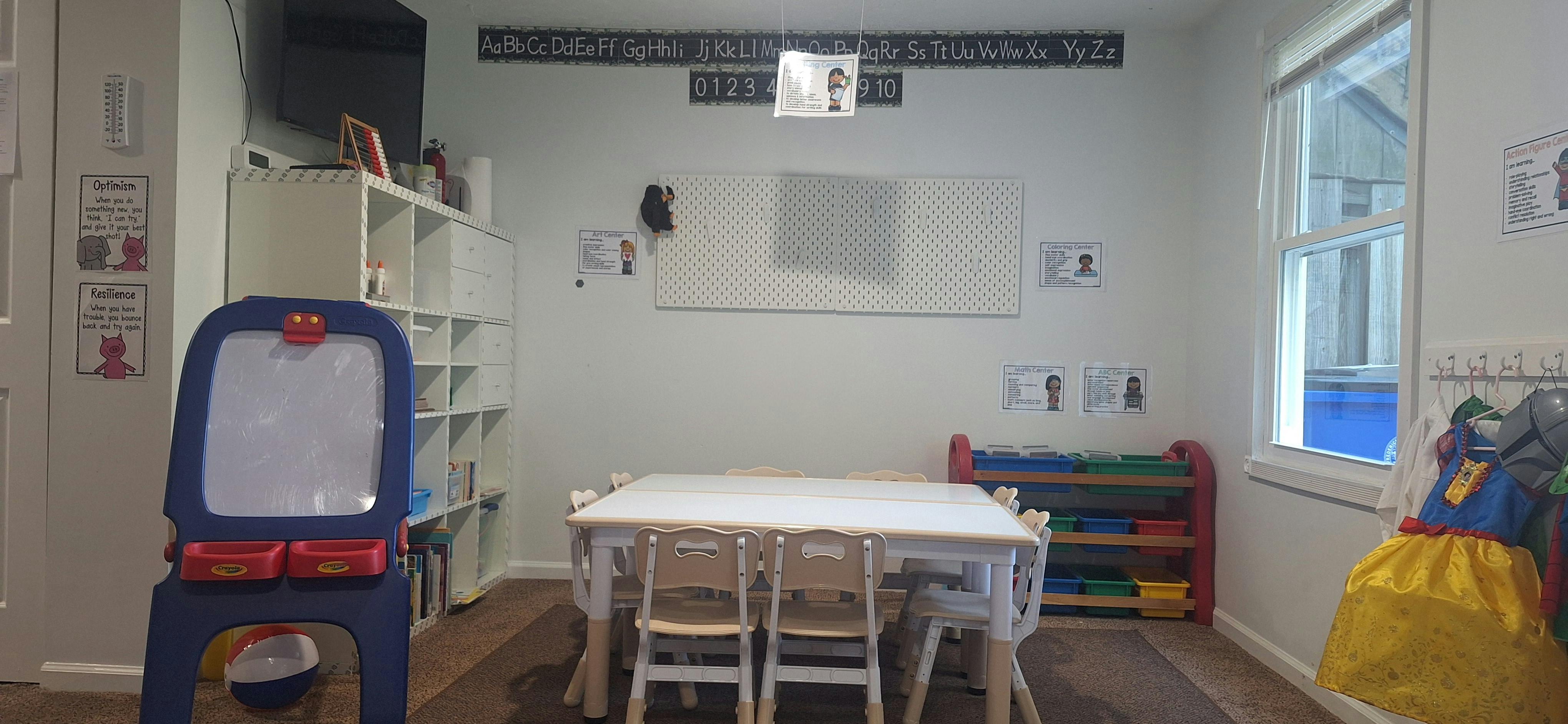 Classroom with child-sized table and chairs, easel, storage shelves, and learning posters