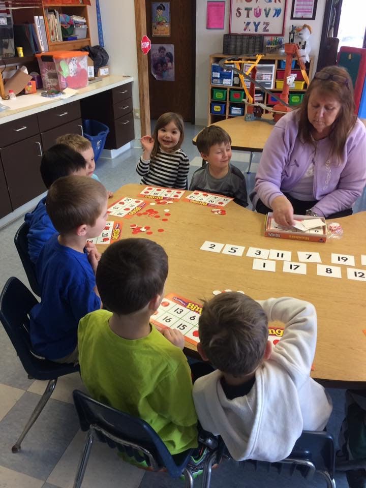 Adult and children playing a game at a table in a classroom