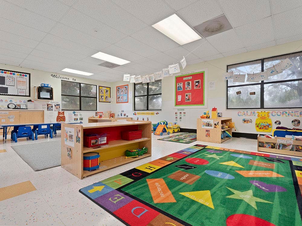 Colorful classroom with educational rugs, shelving units, small tables, and chairs