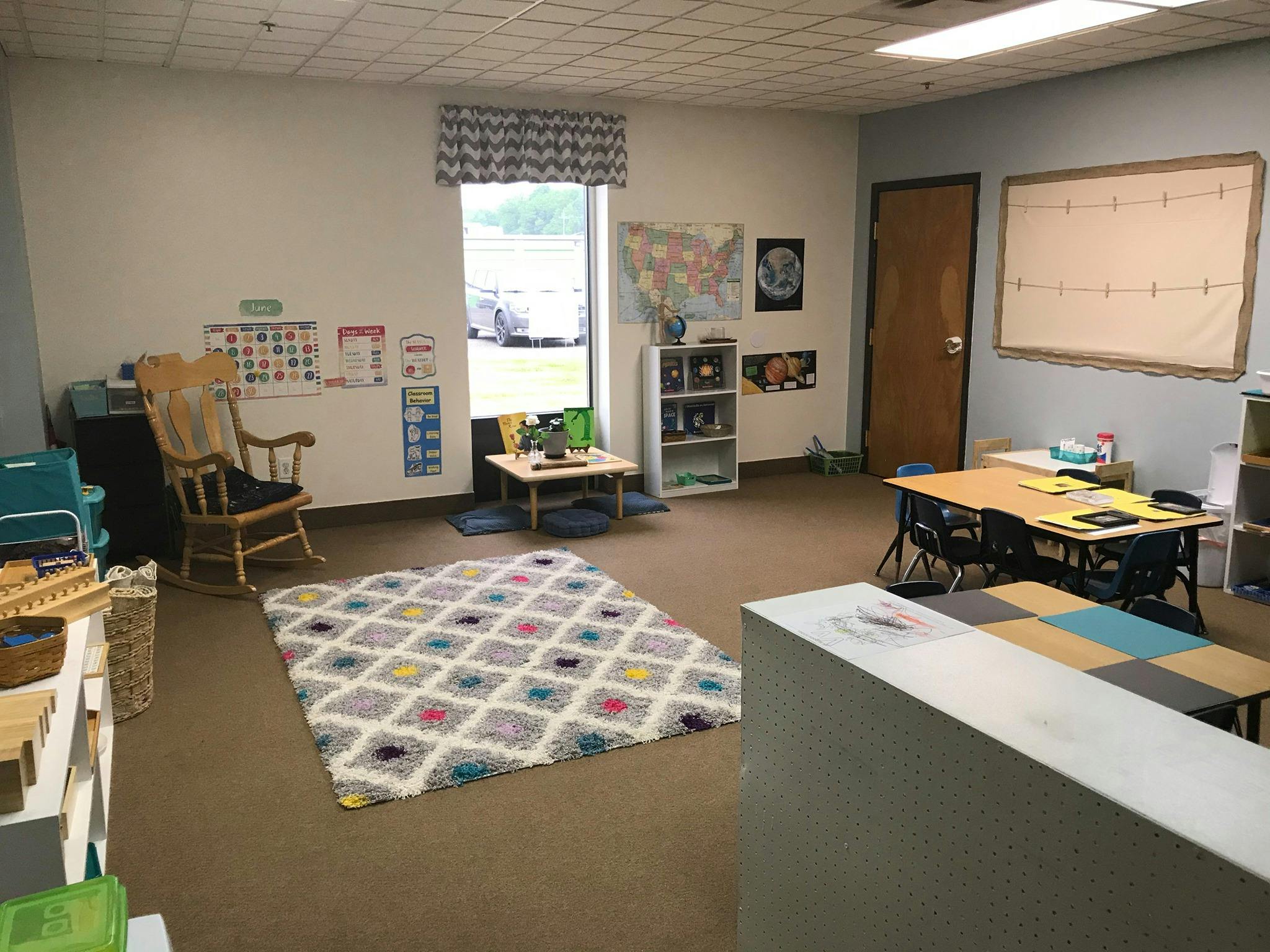 Classroom with a patterned rug, small tables, and a rocking chair