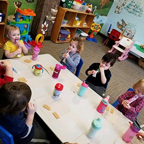 Children sitting at a table with bottles and snacks