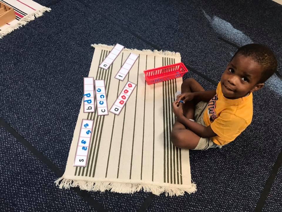 Child sitting on floor next to alphabet cards on a mat