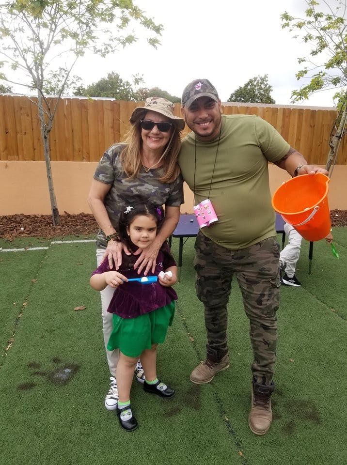 Two adults and a child standing on grass, one adult holding an orange bucket