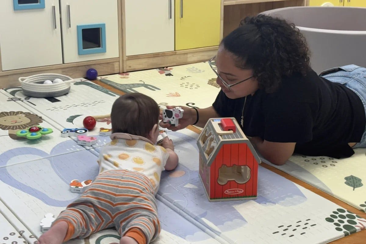 Person on floor showing a toy cow to a child on a playmat