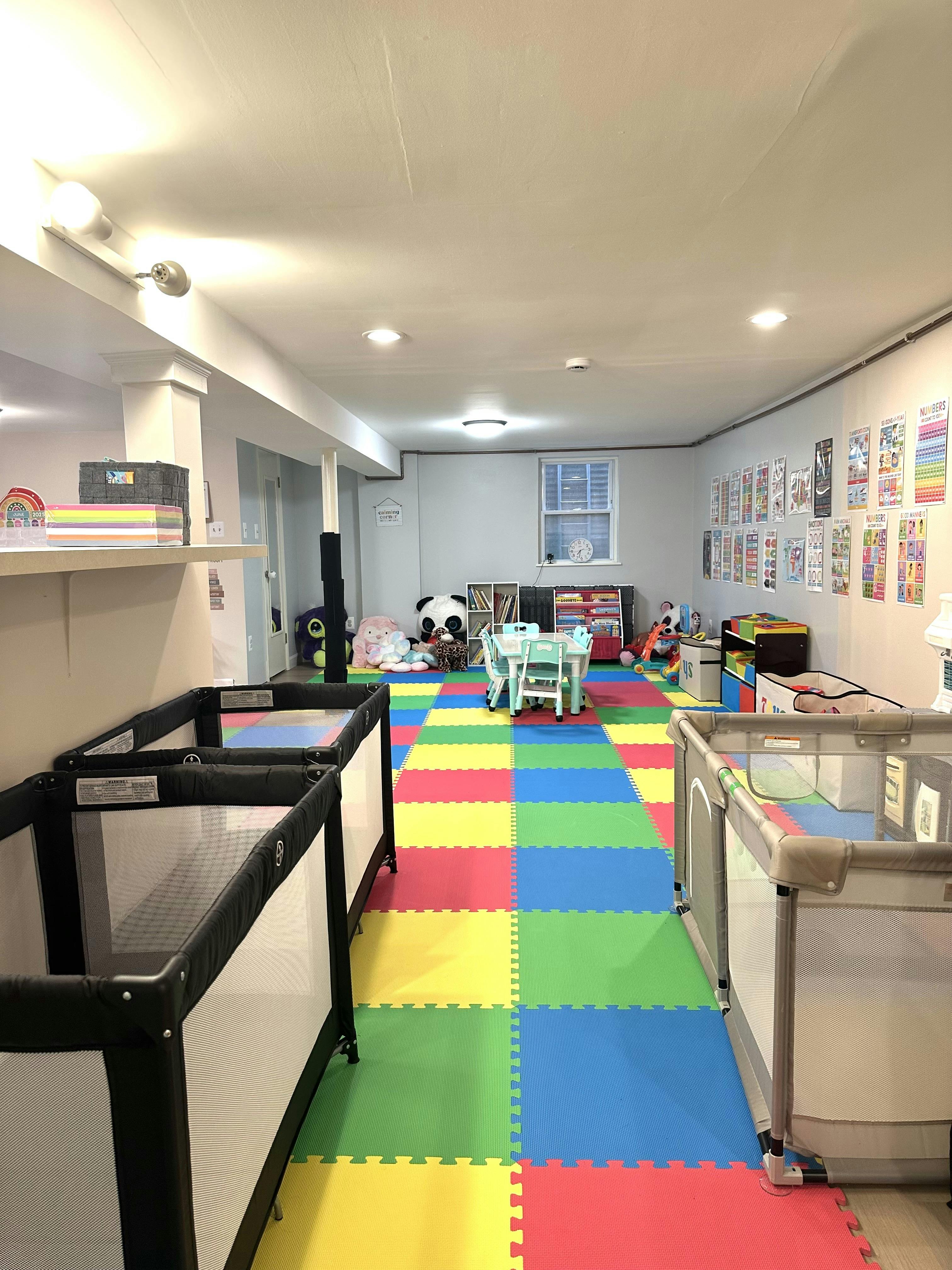 A childcare room with colorful foam floor tiles, cribs, and child-sized furniture