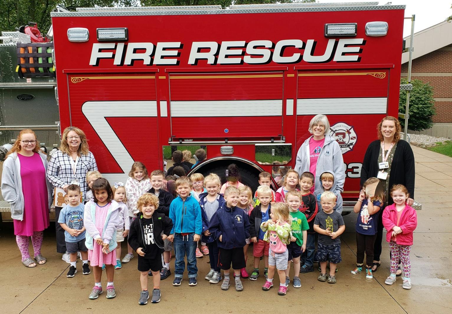 Adults and children standing in front of a fire truck with "FIRE RESCUE" on the side