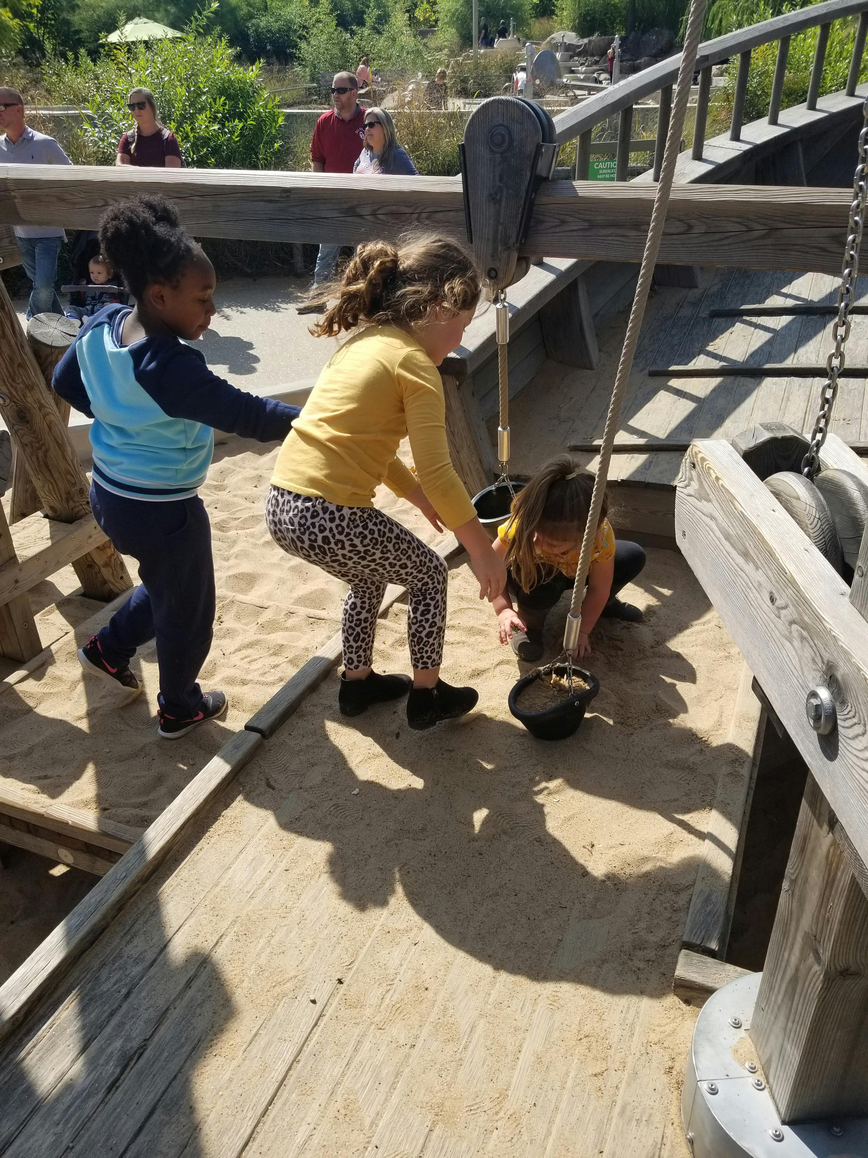 Three children playing in a sandbox with a pulley system