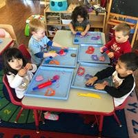 Four children and one adult at a table with trays of colorful objects