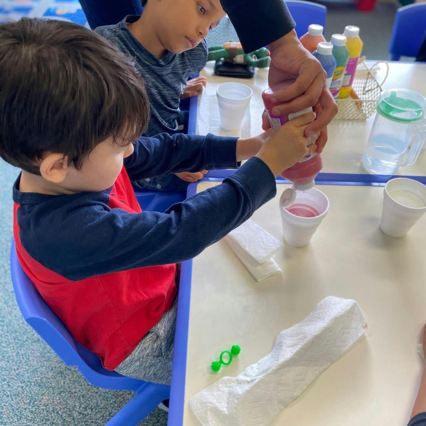 Child squeezing liquid from a bottle into a cup with help from an adult