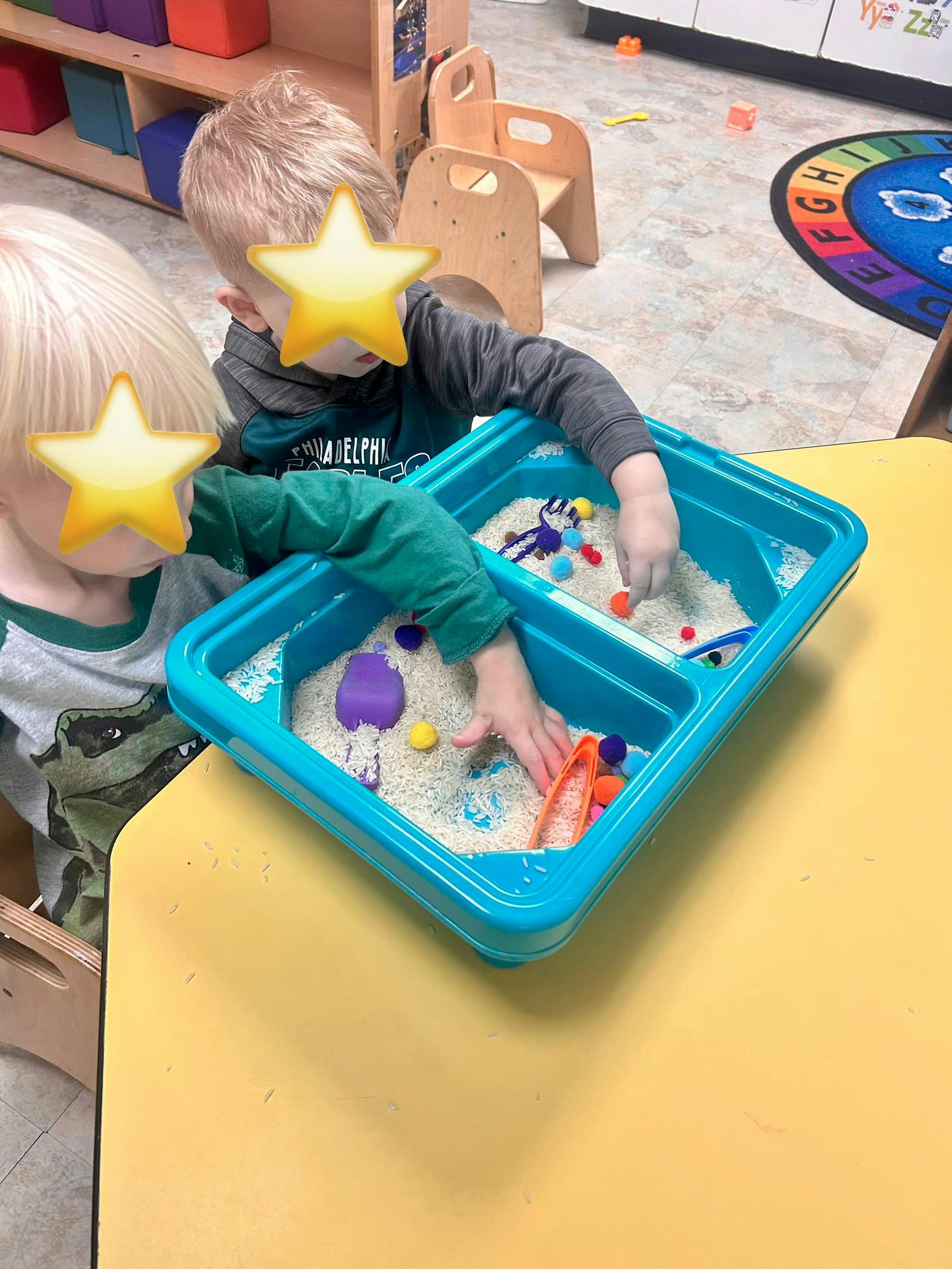 Two children playing with rice and colorful pom-poms in a sensory bin