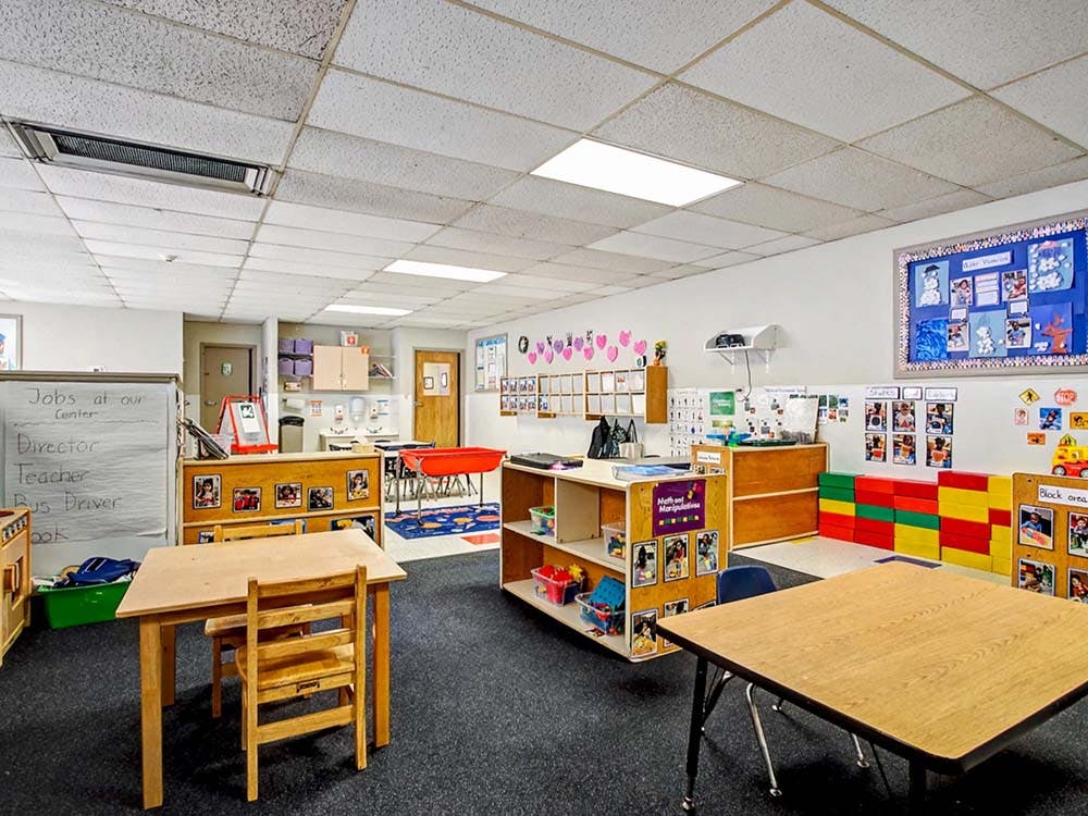 Empty classroom with small tables and chairs, shelves, and bulletin boards