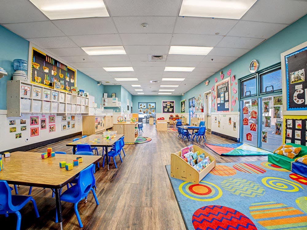 Classroom with small tables and chairs, colorful rugs, and educational displays