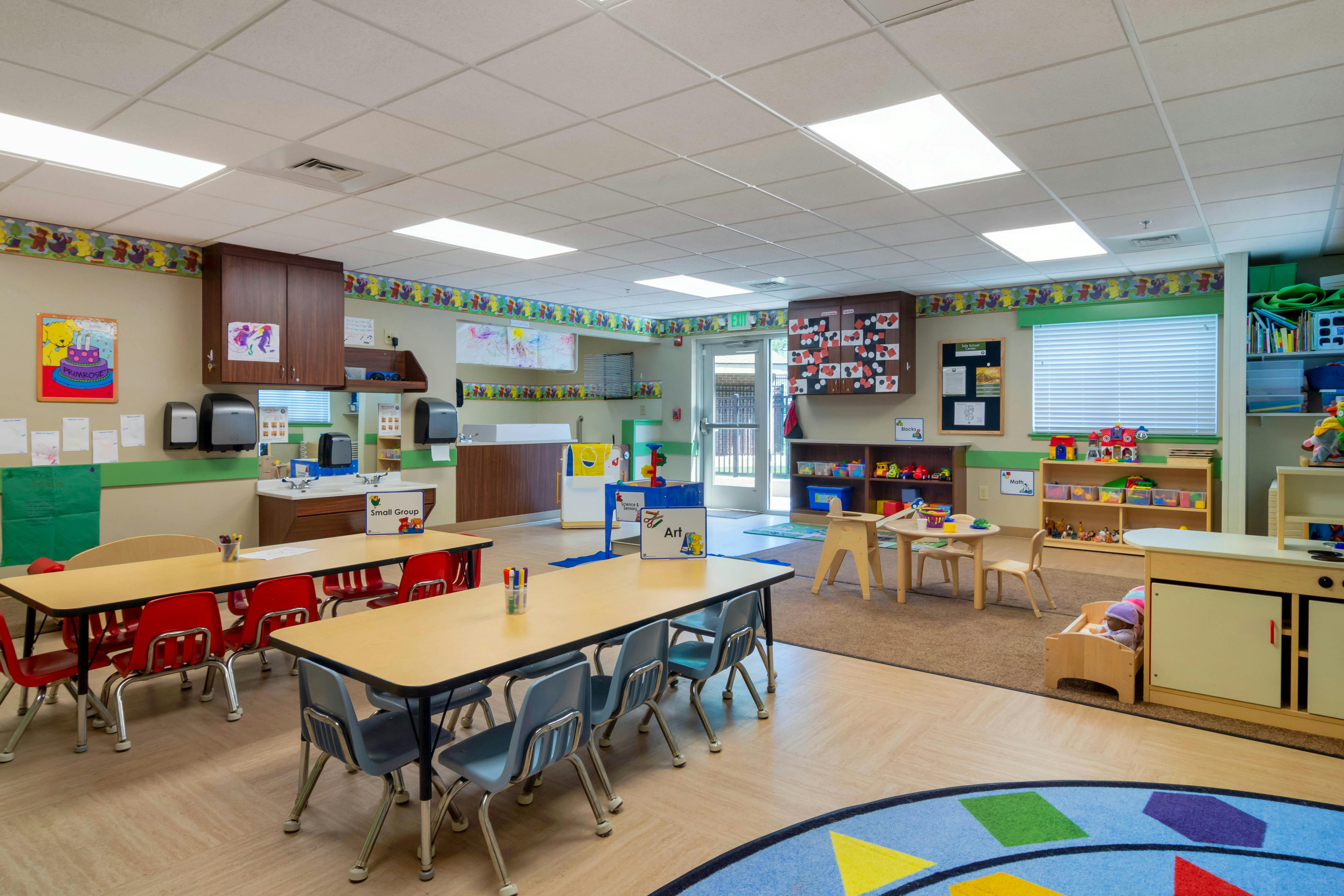 An empty classroom with small tables and chairs, play areas, and a sink