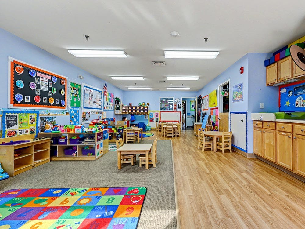 A colorful classroom with small tables and chairs, toys, and learning decorations