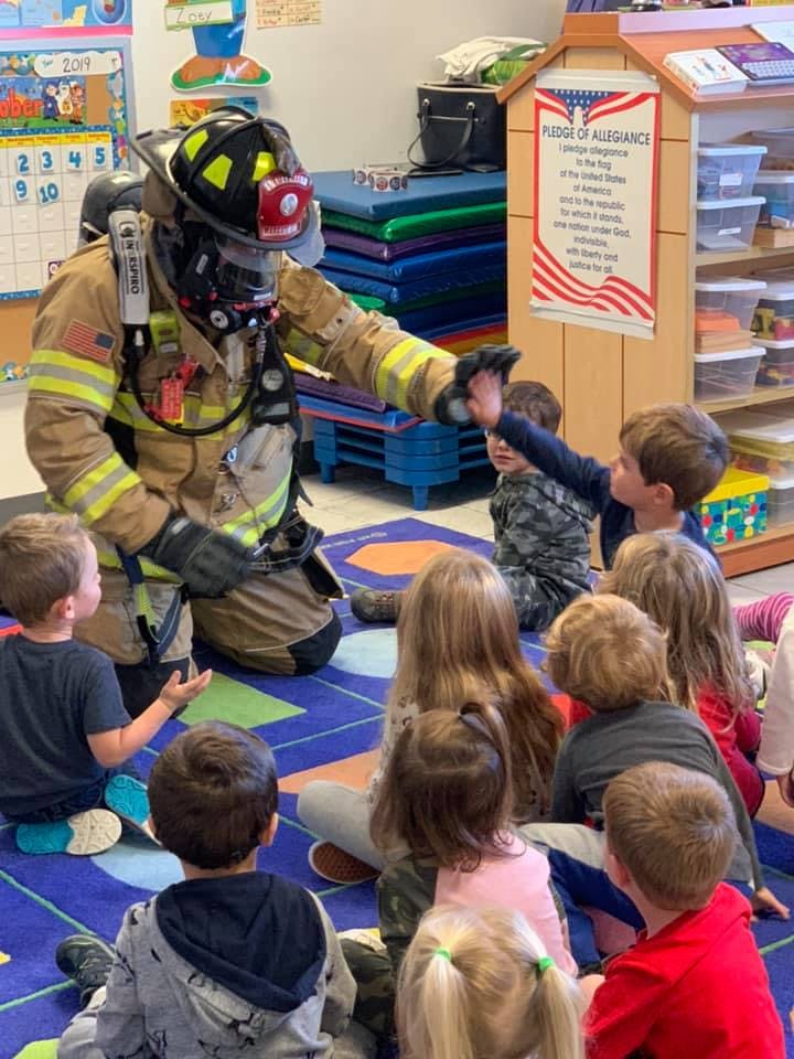 Firefighter in full gear interacting with children in a classroom