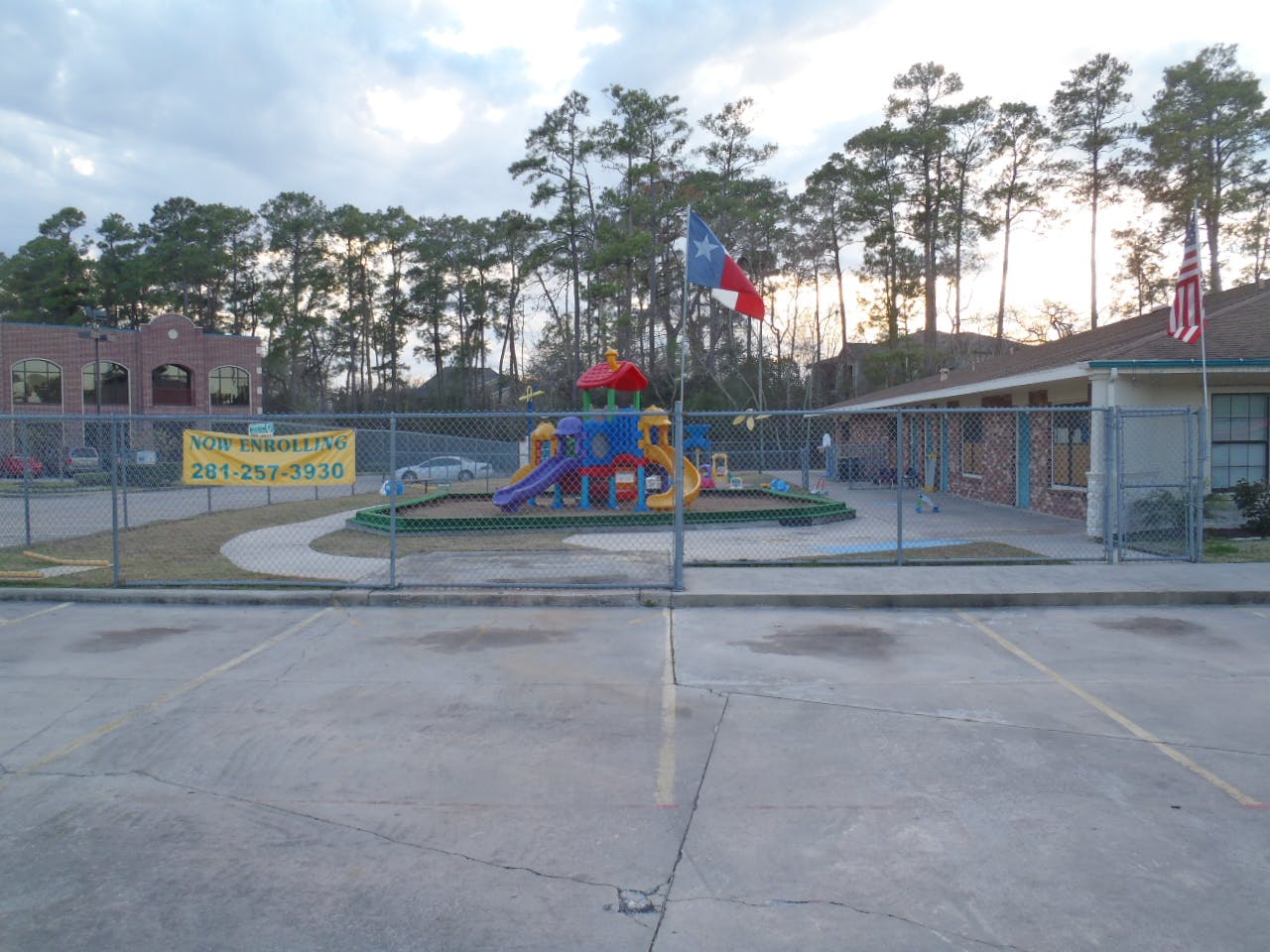 Playground with colorful equipment behind a fence, with flags and buildings
