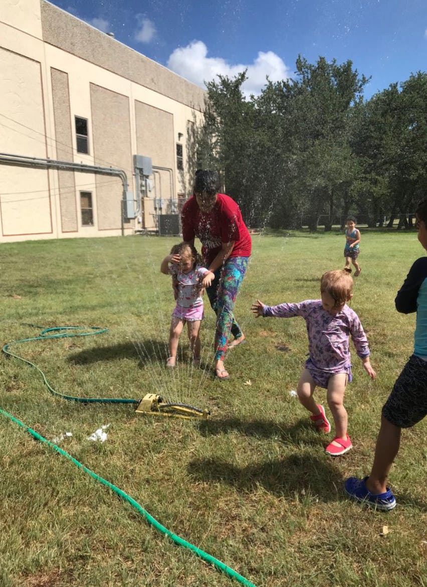 Adult and children playing in a sprinkler on grass