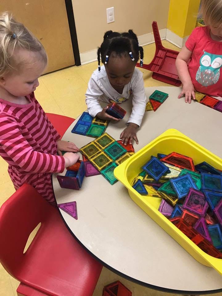 Three children playing with colorful magnetic tiles at a table
