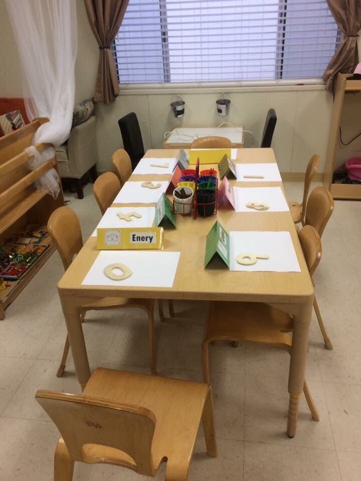 Classroom table set with papers, wooden shapes, and art supplies