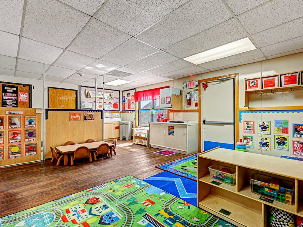 An empty early childhood classroom with a small table and chairs and colorful rugs