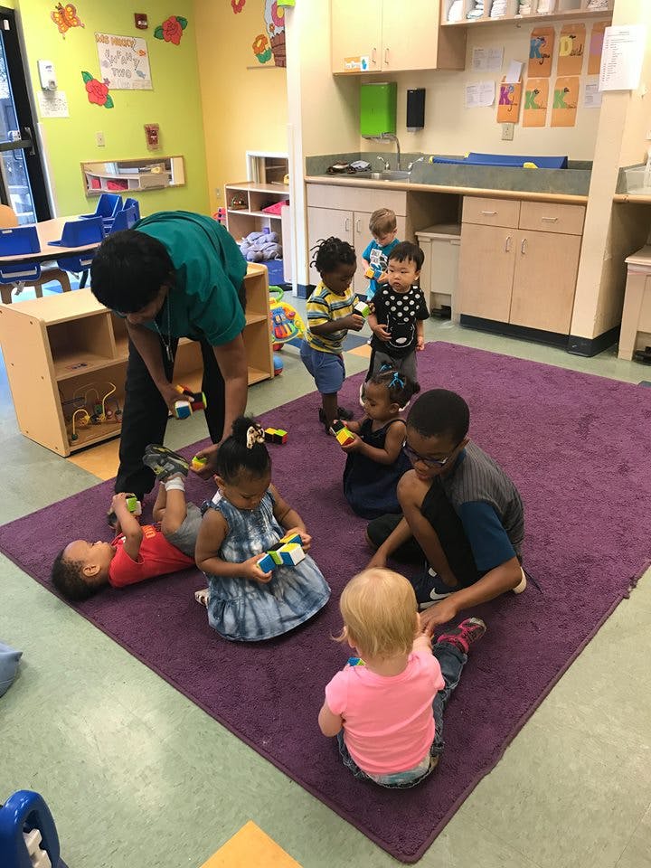Adult and children playing with toys on a purple rug in a classroom