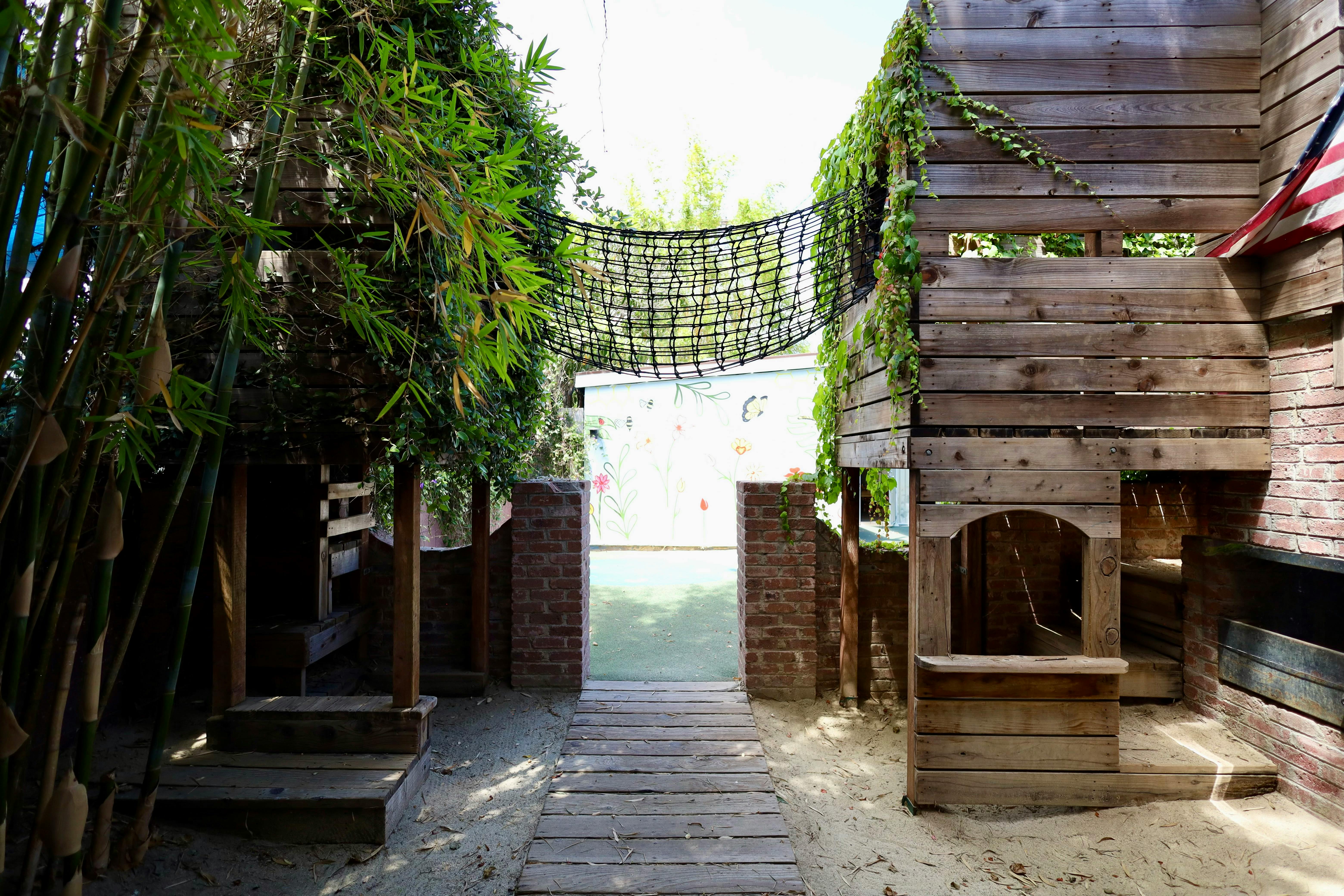 Wooden play structure with a net bridge connecting two sides, bamboo on the left