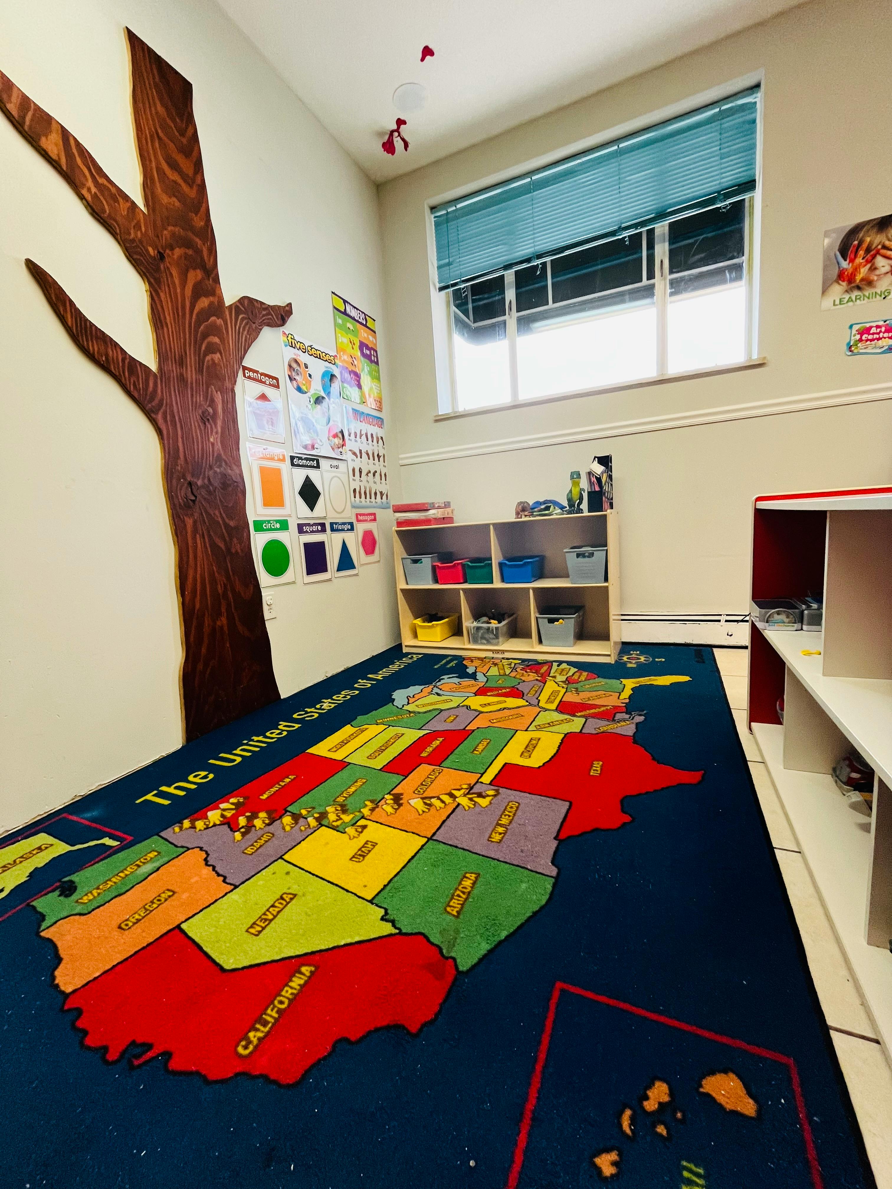 Classroom with a tree mural, map rug, and shelves