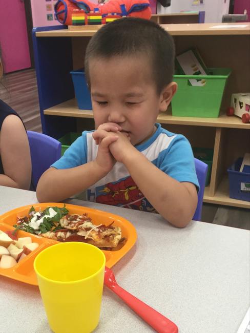 Child sitting at a table with hands clasped before a meal