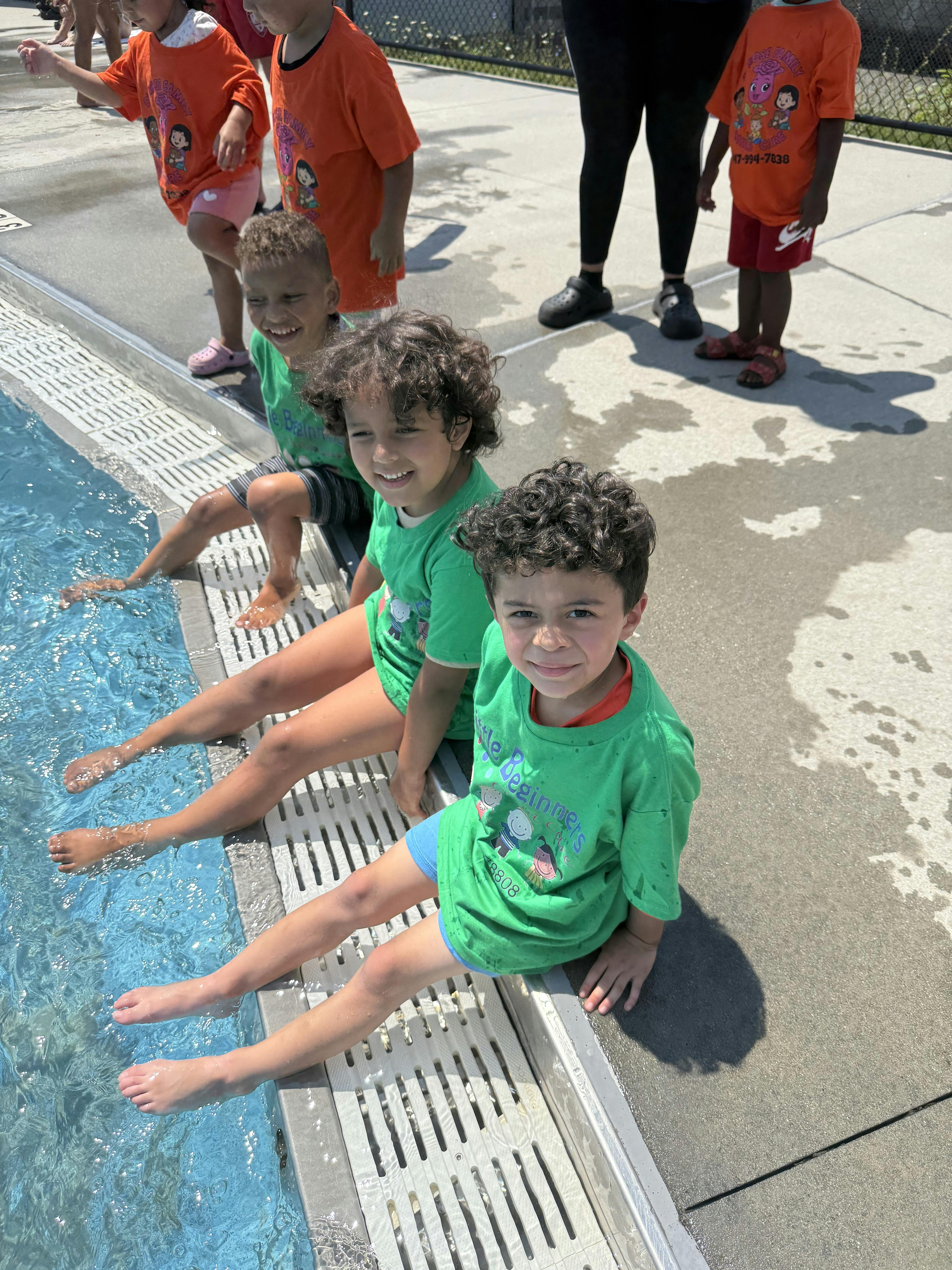 Children wearing matching green shirts sitting by a swimming pool edge