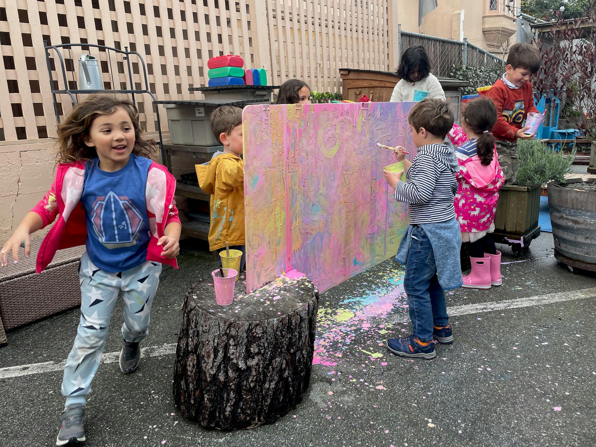 Children playing with chalk on a large board outdoors