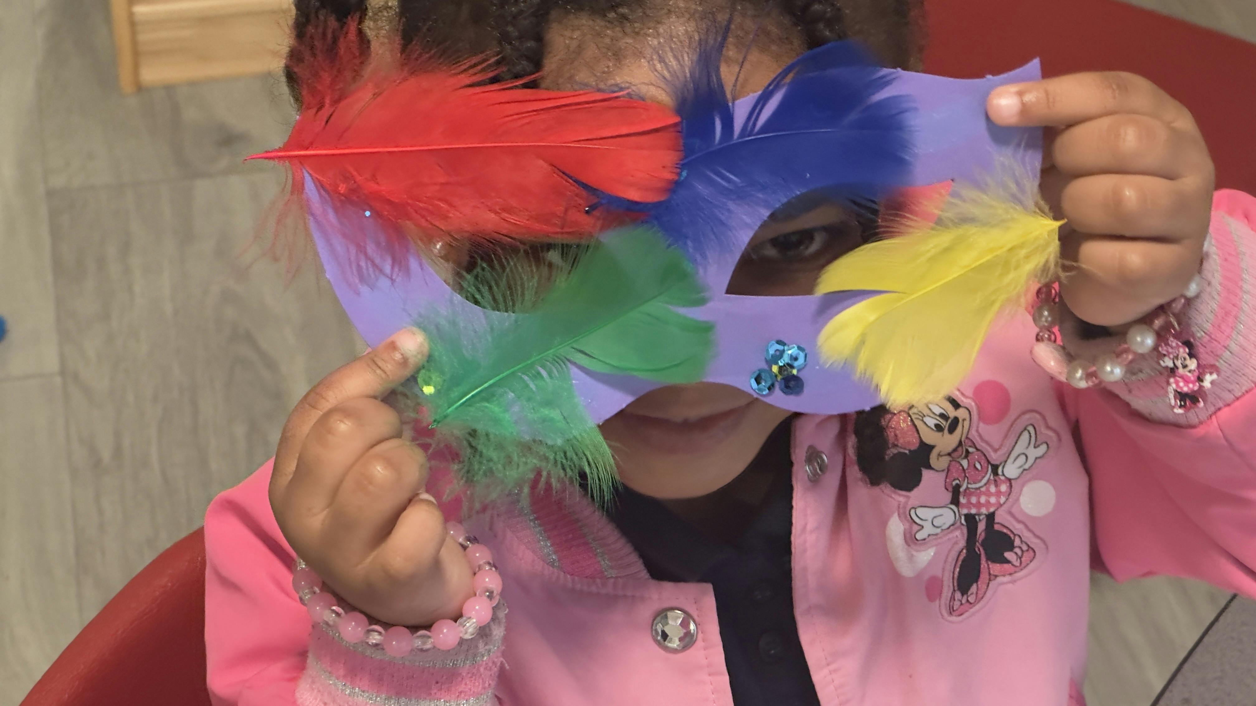 Child peeking over a colorful feather mask